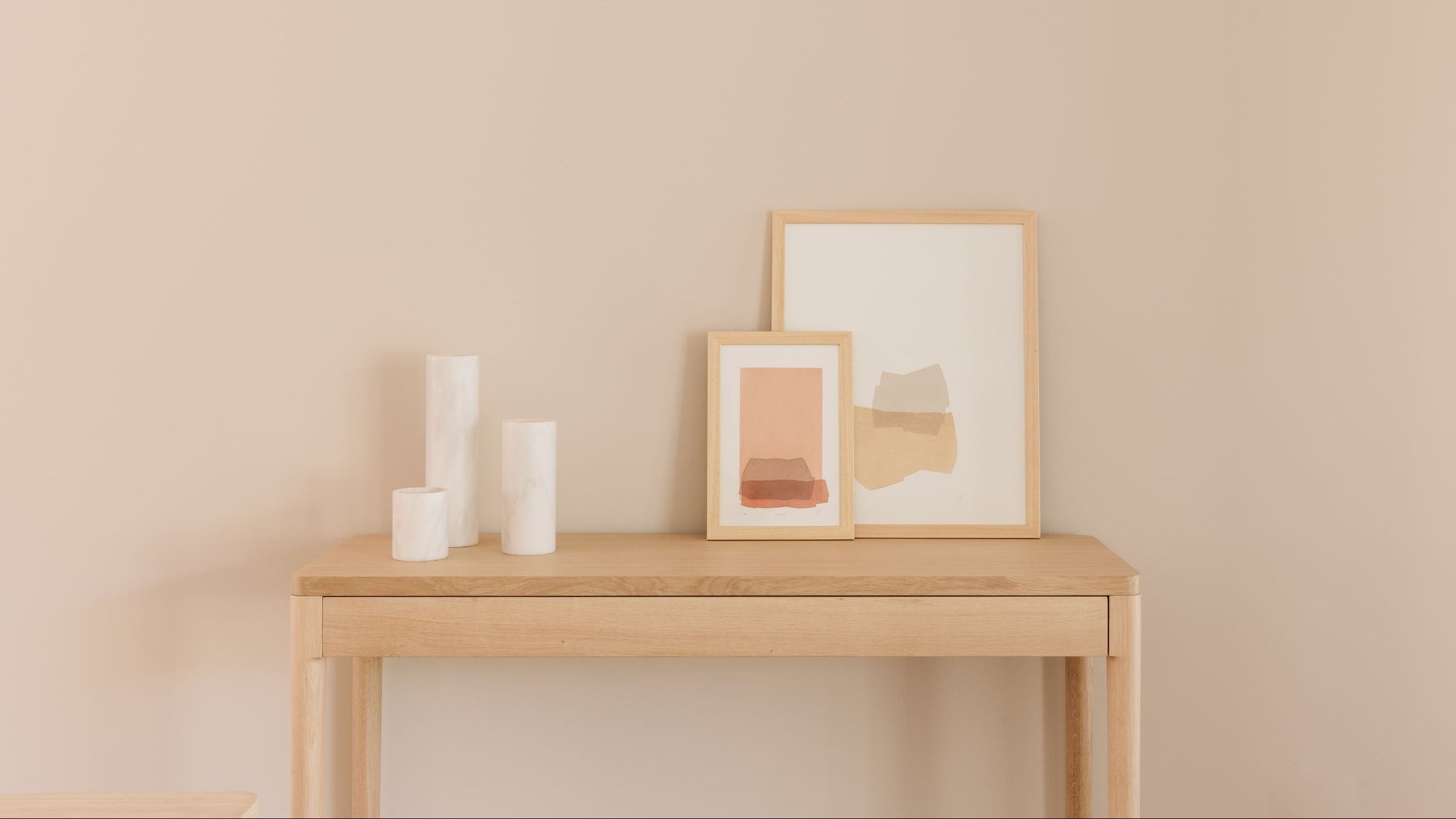 Wood sideboard table with framed artwork and candles against a beige wall