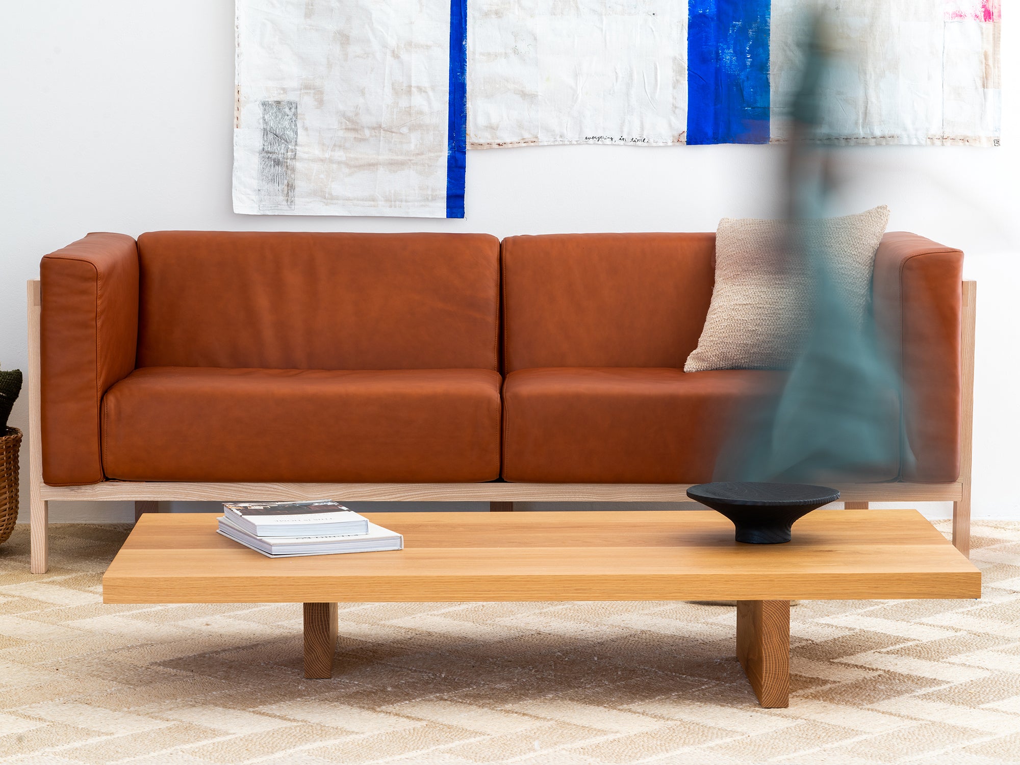 Brown leather sofa in a living room with a wooden coffee table and abstract art on the wall.