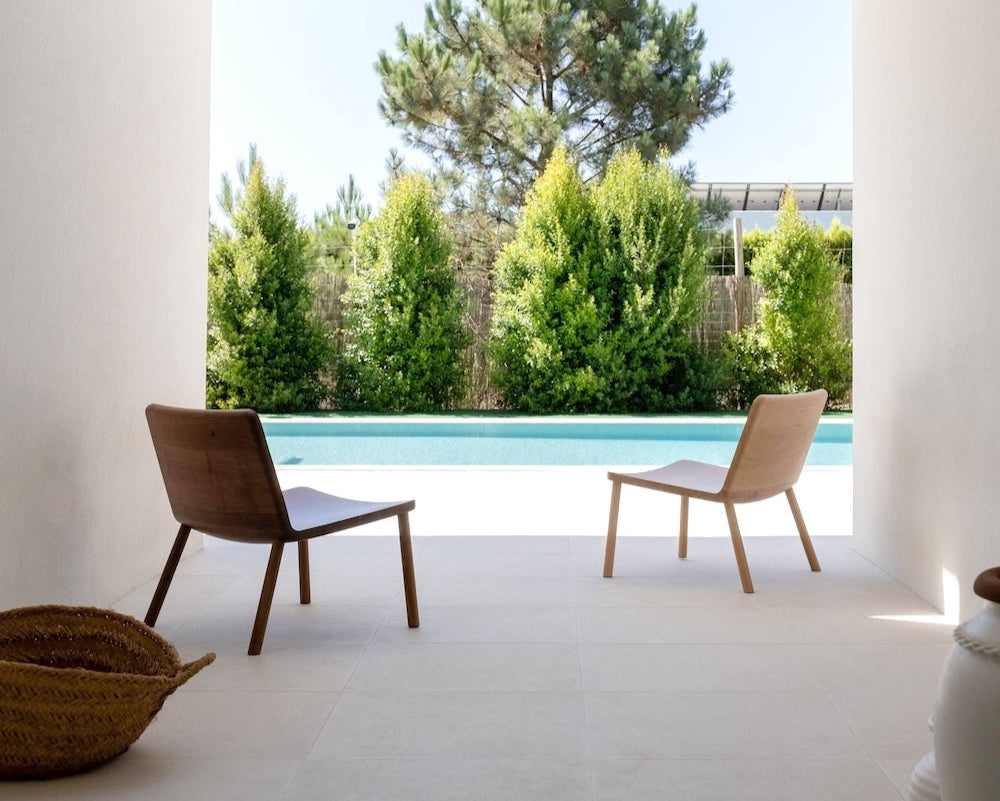 Modern patio with two chairs and a view of trees and pool.