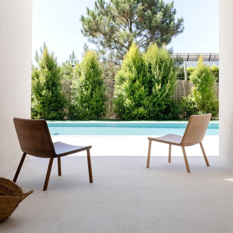 Modern patio with two chairs and a view of trees and pool.